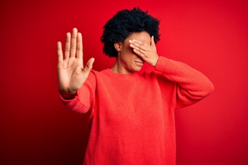 Obraz na płótnie Canvas Young beautiful African American afro woman with curly hair wearing casual sweater covering eyes with hands and doing stop gesture with sad and fear expression. Embarrassed and negative concept.