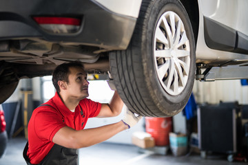 Portrait of a mechanic repairing a lifted car at station
