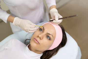 Marking eyebrows with a pencil. Permanent makeup, tattooing of eyebrows. Cosmetologist in white gloves applying make up for woman in beauty salon