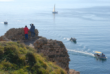 travel concept of people standing on ancient ruins observing beautiful sea with sailing boats...