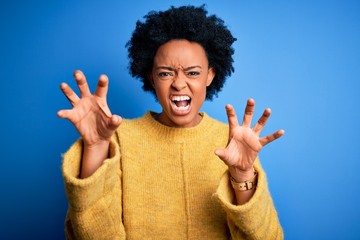 Young beautiful African American afro woman with curly hair wearing yellow casual sweater smiling funny doing claw gesture as cat, aggressive and sexy expression