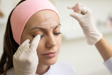 The girl beautician marks with the help of thread eyebrow tattoo. Permanent makeup. Permanent tattooing of eyebrows.