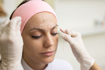 The girl beautician marks with the help of thread eyebrow tattoo. Permanent makeup. Permanent tattooing of eyebrows.