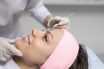Permanent makeup, tattooing of eyebrows. Cosmetologist in white gloves applying make up for woman in beauty salon