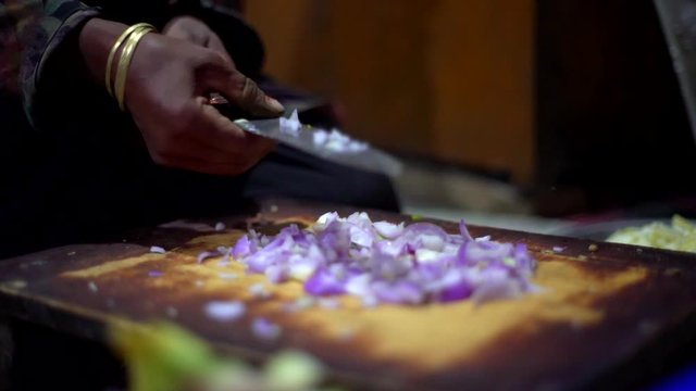 Dark skin woman chopping purple onions, golden bracer big knife as preparing ingredients in a traditional old kitchen. 