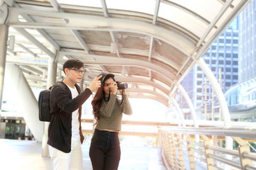 Young Asian tourist couple traveling together. Travelers with backpack and camera explore new downtown city, happy lover taking photo to keep in good memory during their journey trip. Concept of trave
