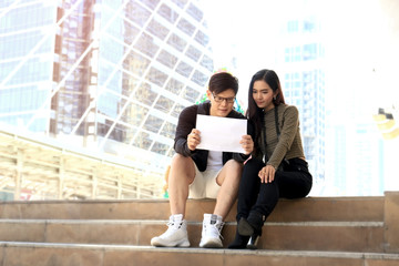 Young Asian tourist couple traveling together. Travelers with backpack holding a map and discussing...