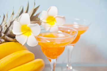 Glasses of tropical exotic multifruit juice cocktail drink with plumeria frangipani flower. Troical beach picnic concept.