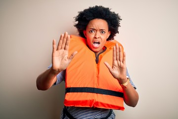 Young African American afro woman with curly hair wearing orange protection lifejacket afraid and terrified with fear expression stop gesture with hands, shouting in shock. Panic concept.