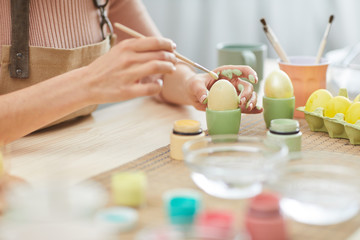 Obraz na płótnie Canvas Close up of unrecognizable young woman painting eggs in pastel colors for Easter while sitting at table in kitchen or art studio, copy space