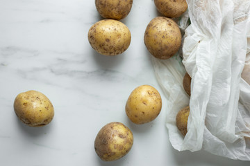 Fototapeta premium fresh bio organic potatoes in recyclable bag on white marble background with copy space