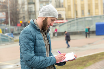 Young man makes records of research or questioning against the background of a city street. Public opinion poll, collection of statistical data, questioning.