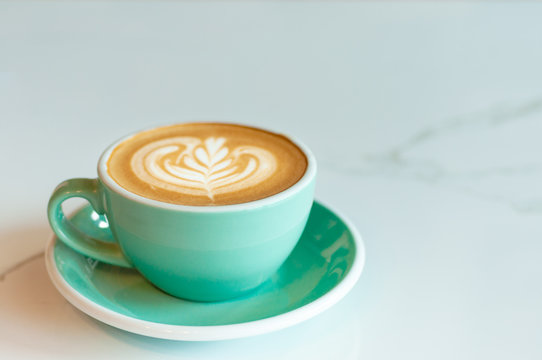 Fresh latte coffee in green cup on marble table with copy space.