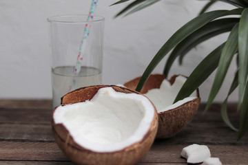 two halves of a coconut on a wooden table and a glass with coconut water