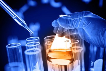 Flask in scientist hand with lab glassware background