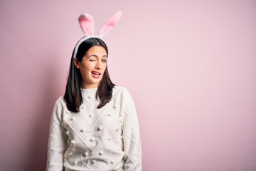 Young caucasian woman wearing cute easter rabbit ears over pink isolated background winking looking...