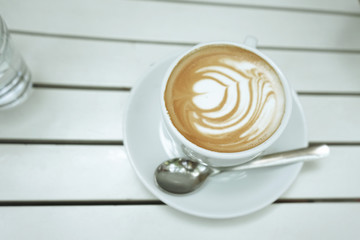 A cup of coffee with heart pattern in a white cup on white wooden background