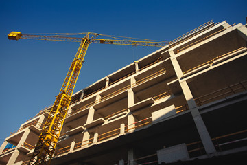 Modern building industry concept. Construction site with yellow crane on blue sky background. Sunny...