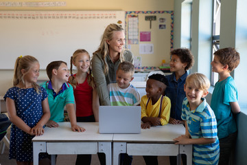 Female teacher using a laptop computer with of schoolchildren