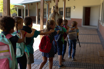 Female teacher with group of schoolchildren walking a outside corridor at an elementary school