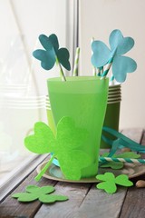  St. Patrick's Day, green glasses, straws with a decorative shamrock, clover on a wooden surface on a window background, getting ready for a party