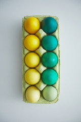 Fototapeta na wymiar Above view of green and yellow hand painted Easter eggs in crate arranged in minimal composition on white background, copy space