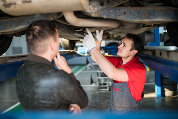 Car mechanic and customer stand next to the serviced car and looking through the checklist. The car had an annual checkup and stands in the garage