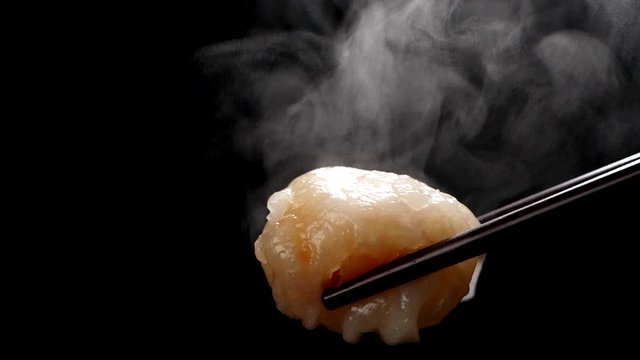 Shrimp Dumpling (Ha gow) on chopsticks with steam in slow motion on black background