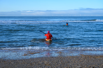 Unidentified people in kayaks going in to water on North sea sandy beach during low tide near Castricum aan Zee, Netherlands