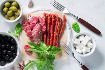 Set of chorizo sausages with olives and a sprig of basil. Antipasti snack.