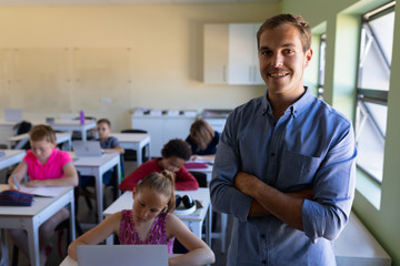 Male school teacher standing with arms crossed in an elementary school classroom