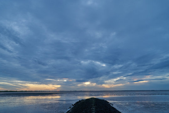 scenic dramatic sunset sky with dark clouds over the bay Jadebusen in Sehestedt (community Butjadingen, district Wesermarsch, Germany) over a groyne in the mud flat during low tide