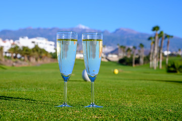 Two glasses with  bubbles white champagne or cava wine served on green golf club grass with mountains view during golf competition event or celebration