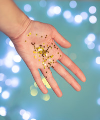 Shiny tiny golden stars in open human palms on a blue background with bokeh. Festive decor, Christmas, New Year.