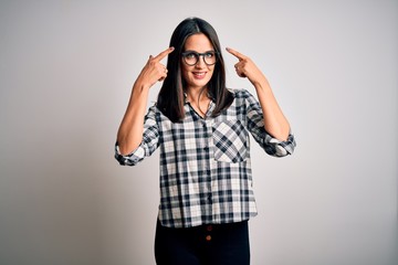 Young brunette woman with blue eyes wearing casual shirt and glasses over white background smiling pointing to head with both hands finger, great idea or thought, good memory