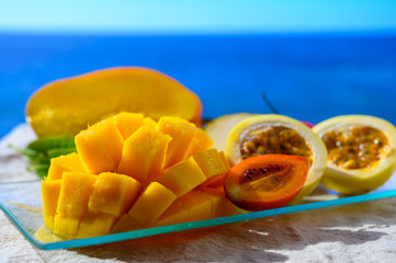 Exotic fruits, fresh ripe sweet yellow mango and passion fruits served on glass plate with blue seaview background