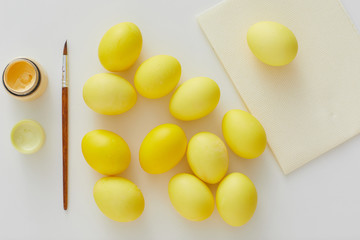 Above view of pastel yellow Easter eggs with paint brush arraigned in minimal composition on white background, copy space