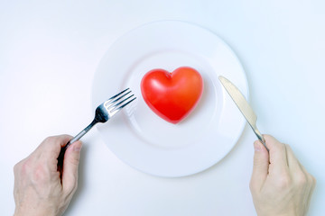 Men's hands hold a knife and a fork. Red heart and measuring tape on a plate on a white background. Healthy eating concept.