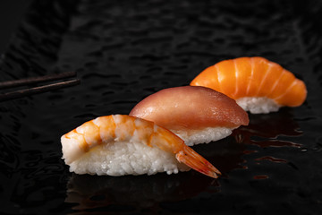 Obraz na płótnie Canvas Nigiri sushi set with shrimp, salmon and tuna on black glossy plate, selected focus
