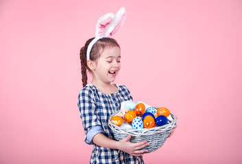 Portrait of a cute little girl with an Easter egg basket on an isolated pink background.