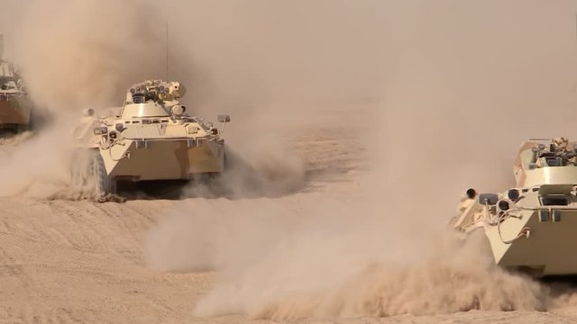 A military column of armored vehicles moves through the desert, raising dust. Special operation of the military