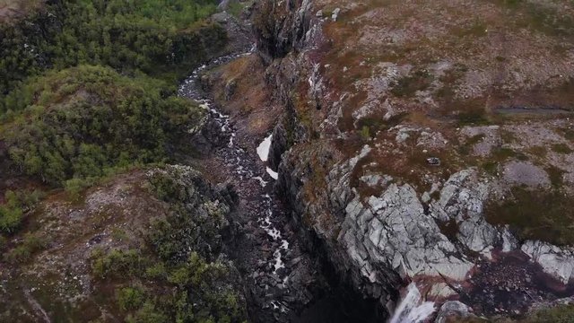 Aerial, tilt, drone shot over a waterfall, towards the Sautso canyon, on a dark, overcast day, in Alta, Finnmark, north Norway