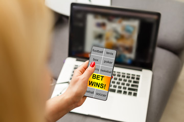 Close up cropped shot of female hands holding smartphone with bookmaker's website on a screen. Young woman placing sport bets online using mobile application.