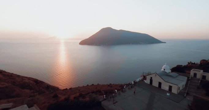 Drone panoramic aerial view of sunset in the Mediterranean sea in Lipari, Sicily. Drone is flying above houses to a stunning cliff seascape. It's showing the volcano with sunset crazy colors