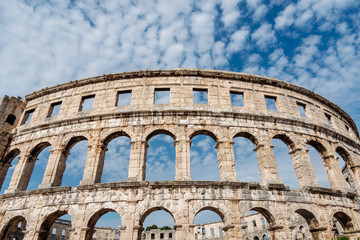 Fototapeta premium Exterior facade of the historic Roman Empire gladiator amphitheatre Coliseum and blue sky with beautiful white clouds on the background, Pula, Croatia. 