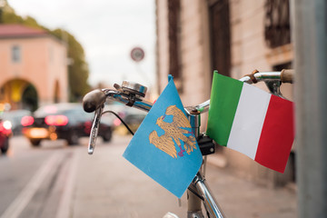 Small Italian flag and Fiuli's flags on a parked bicycle in Piazza Primo Maggio, Udine....