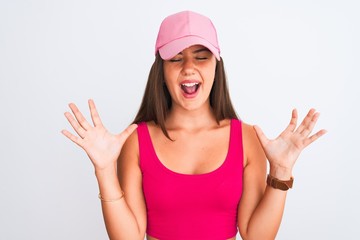 Obraz na płótnie Canvas Young beautiful girl wearing pink casual t-shirt and cap over isolated white background celebrating mad and crazy for success with arms raised and closed eyes screaming excited. Winner concept
