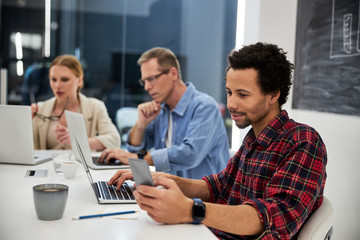 Afro american guy using cellphone while working with colleagues