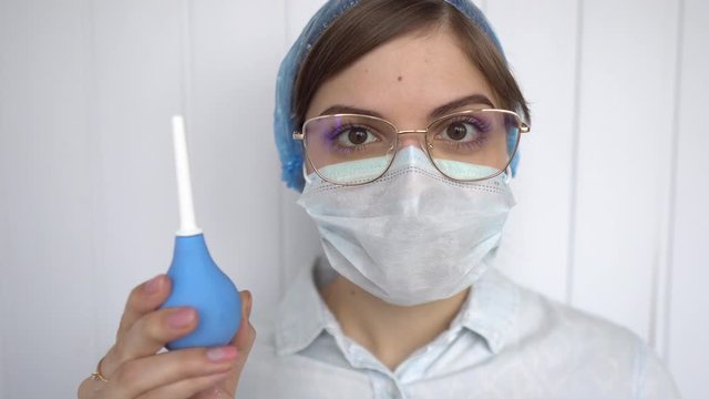 the female doctor shows and clicks on an enema and very focused. protective mask and glasses. non-traditional methods of treatment.