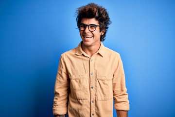 Young handsome man wearing casual shirt standing over isolated blue background looking away to side with smile on face, natural expression. Laughing confident.